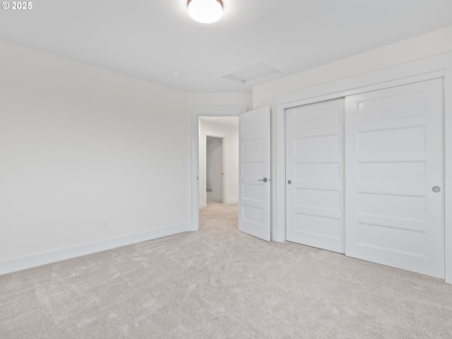 unfurnished bedroom featuring light carpet, attic access, baseboards, and a closet