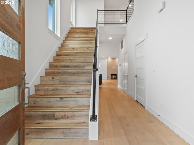 staircase featuring a high ceiling, wood finished floors, visible vents, baseboards, and a lit fireplace