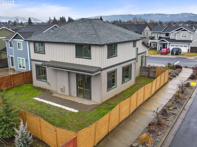 rear view of property with a fenced backyard, a mountain view, a shingled roof, a residential view, and board and batten siding