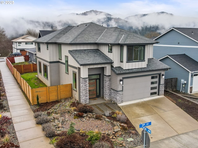 view of front of property with driveway, stone siding, a shingled roof, and fence