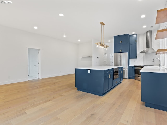 kitchen with light wood finished floors, wall chimney exhaust hood, blue cabinets, stainless steel appliances, and light countertops