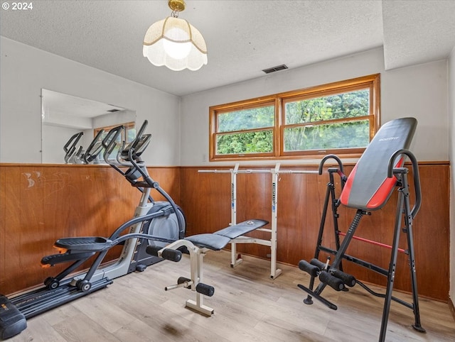 workout room featuring light hardwood / wood-style flooring, a textured ceiling, a healthy amount of sunlight, and wood walls