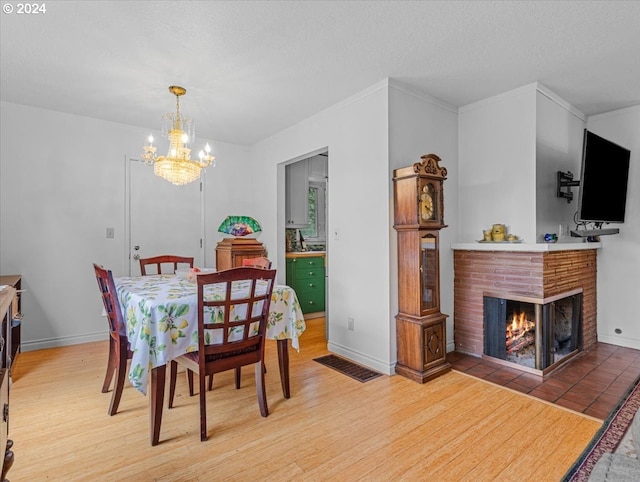 dining area with a notable chandelier, a textured ceiling, wood-type flooring, and a brick fireplace