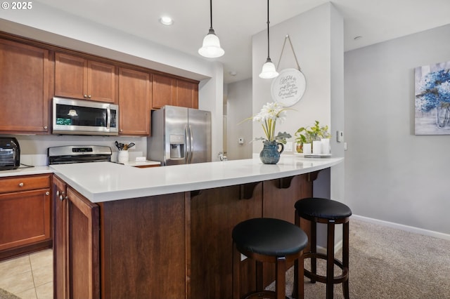 kitchen with a kitchen bar, kitchen peninsula, stainless steel appliances, light colored carpet, and decorative light fixtures