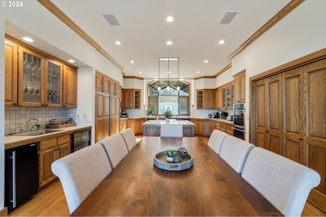 dining area with light wood-type flooring, ornamental molding, sink, and wine cooler