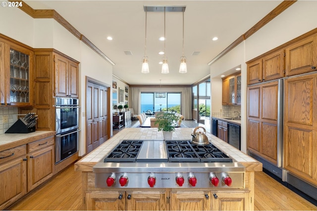 kitchen with backsplash, tile counters, stainless steel appliances, and light hardwood / wood-style floors