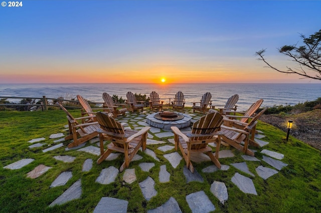 patio terrace at dusk with a water view, an outdoor fire pit, and a lawn