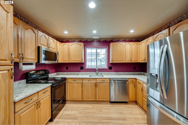 kitchen with light wood-type flooring, sink, stainless steel appliances, and a textured ceiling