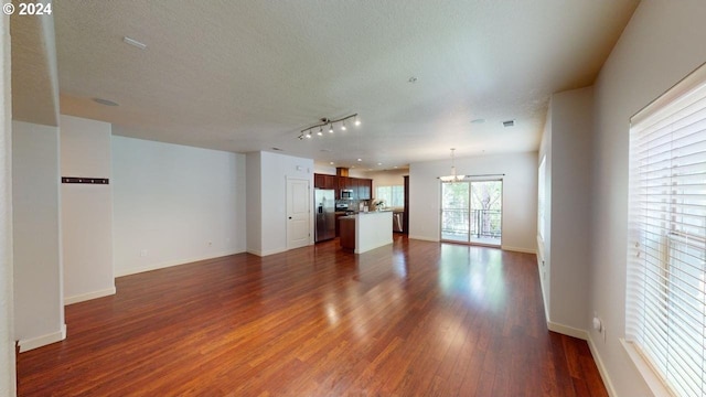 unfurnished living room with a textured ceiling, rail lighting, dark hardwood / wood-style floors, and a chandelier