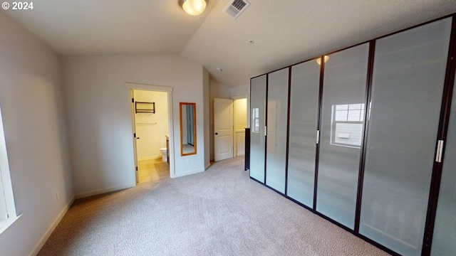 unfurnished bedroom featuring light carpet, lofted ceiling, ensuite bath, and a closet