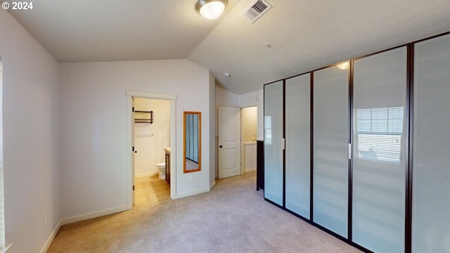 unfurnished bedroom featuring light carpet, lofted ceiling, ensuite bathroom, and a closet