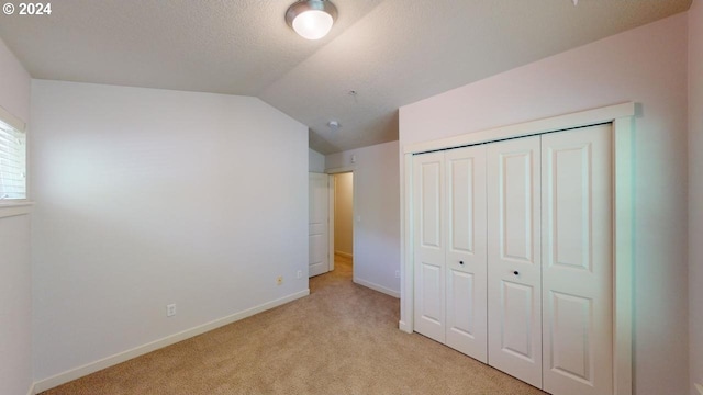 unfurnished bedroom with a closet, light carpet, a textured ceiling, and lofted ceiling