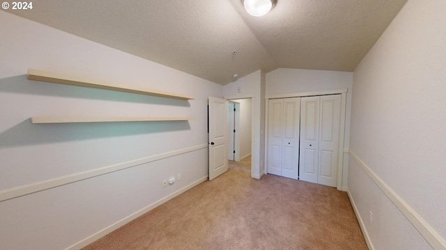 unfurnished bedroom with a closet, a textured ceiling, light colored carpet, and vaulted ceiling