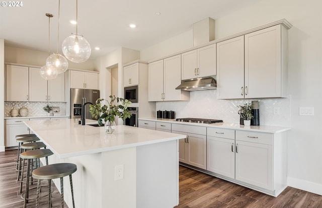 kitchen featuring appliances with stainless steel finishes, dark hardwood / wood-style flooring, a kitchen breakfast bar, a kitchen island with sink, and pendant lighting