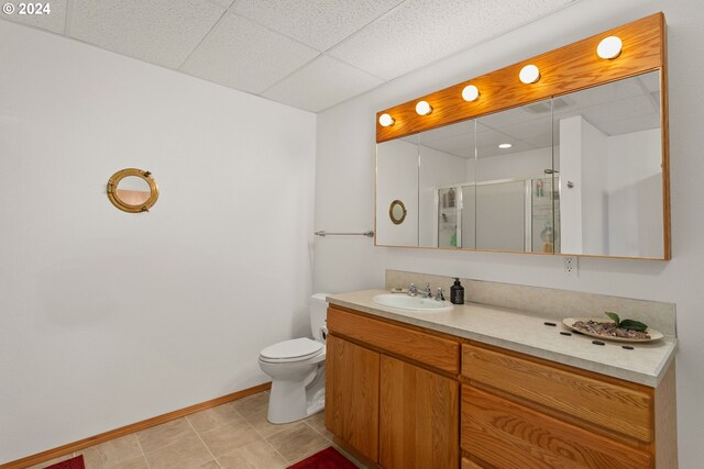 bathroom featuring a shower with door, vanity, tile patterned flooring, toilet, and a paneled ceiling