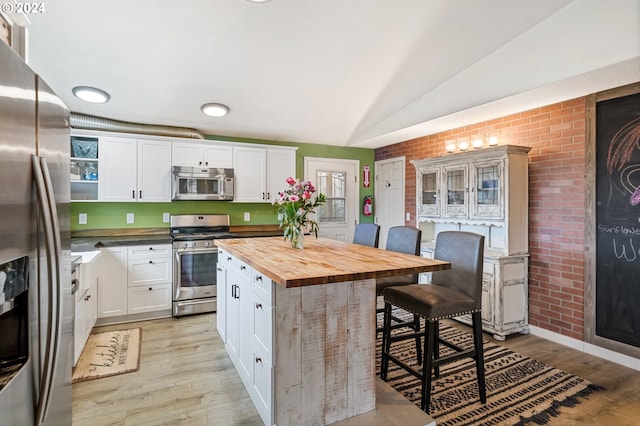 kitchen featuring wooden counters, stainless steel appliances, white cabinets, a center island, and a breakfast bar area