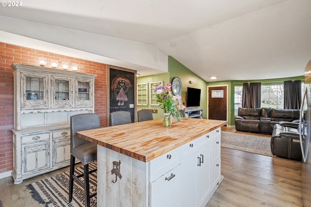 kitchen featuring a breakfast bar, wooden counters, white cabinets, vaulted ceiling, and light wood-type flooring