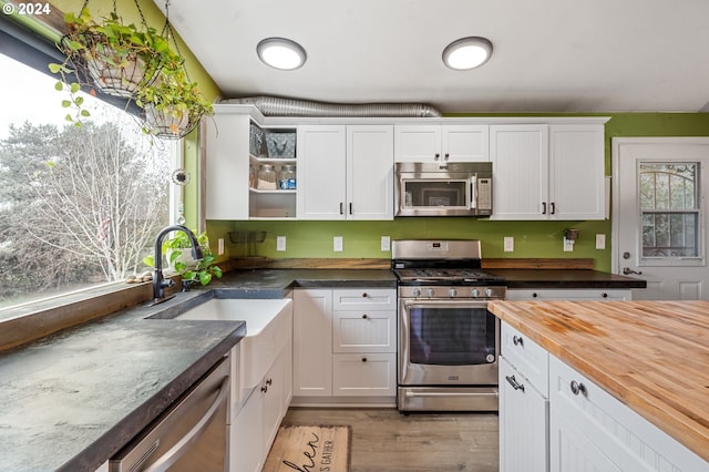 kitchen with stainless steel appliances, butcher block countertops, white cabinetry, and sink