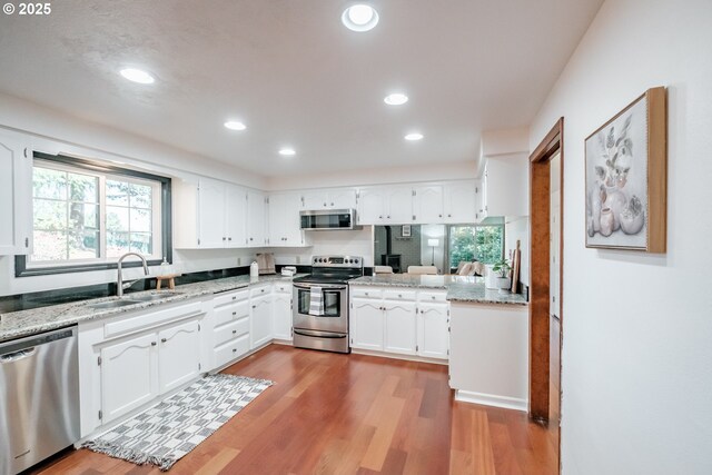 kitchen featuring sink, light stone counters, appliances with stainless steel finishes, light hardwood / wood-style floors, and white cabinets