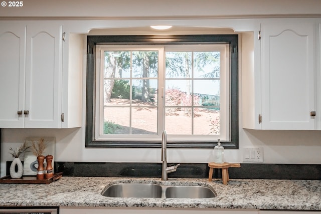 kitchen featuring light stone counters, sink, and white cabinets