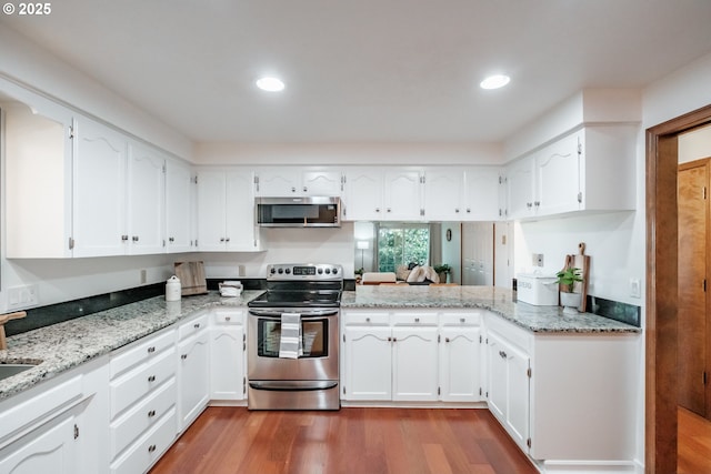 kitchen featuring appliances with stainless steel finishes, white cabinetry, wood-type flooring, kitchen peninsula, and light stone countertops