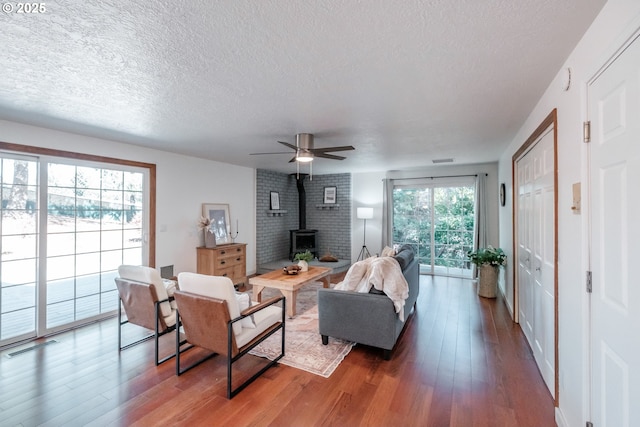 living room featuring hardwood / wood-style flooring, ceiling fan, a textured ceiling, and a wood stove