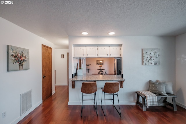 kitchen featuring a breakfast bar area, white cabinetry, light stone counters, stainless steel fridge, and kitchen peninsula