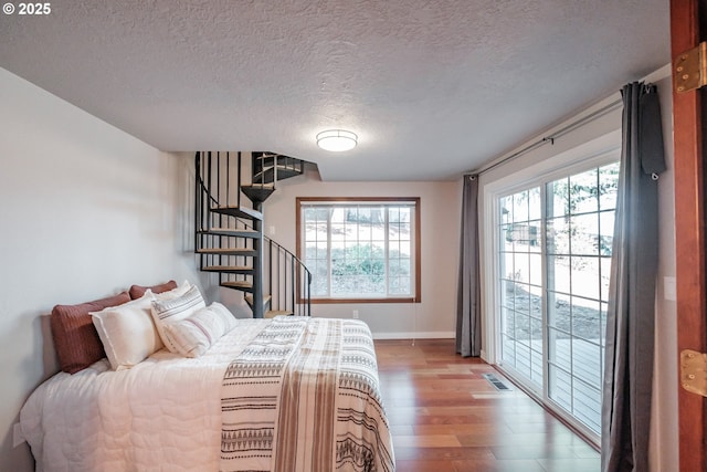 bedroom featuring multiple windows, hardwood / wood-style flooring, access to outside, and a textured ceiling