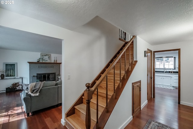 stairs featuring sink, hardwood / wood-style flooring, a textured ceiling, and a brick fireplace