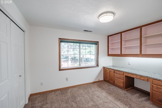 unfurnished office featuring light carpet, built in desk, and a textured ceiling