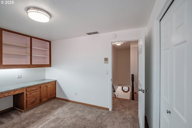 unfurnished office with built in desk, light carpet, and a textured ceiling