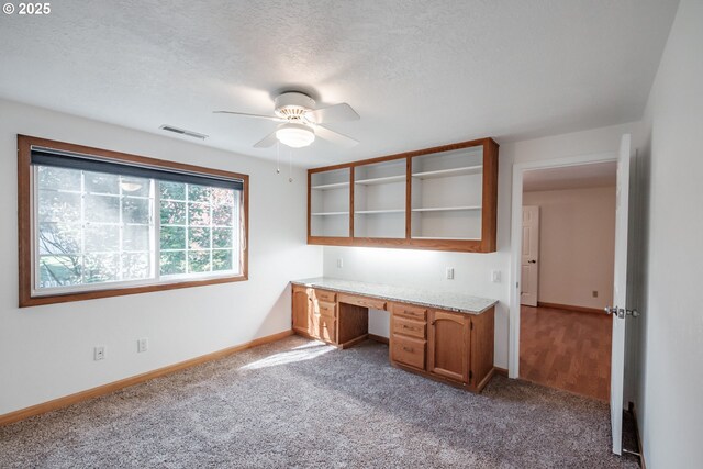 unfurnished office with ceiling fan, built in desk, light colored carpet, and a textured ceiling