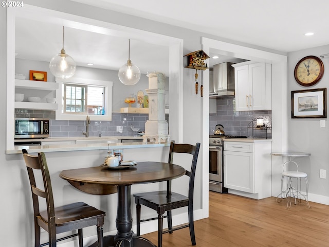 kitchen with white cabinets, hanging light fixtures, wall chimney range hood, and appliances with stainless steel finishes