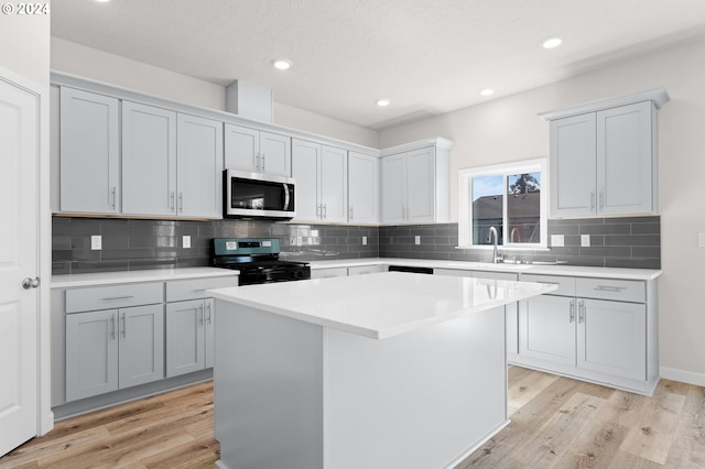 kitchen with a kitchen island, black gas range oven, white cabinetry, light hardwood / wood-style flooring, and backsplash