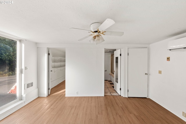 unfurnished room featuring a wall mounted air conditioner, light hardwood / wood-style floors, a healthy amount of sunlight, and a textured ceiling