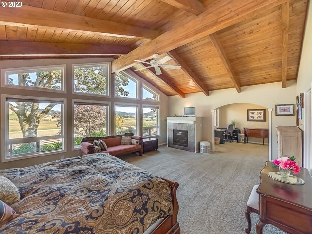 bedroom with wooden ceiling, carpet, a tiled fireplace, ceiling fan, and beam ceiling