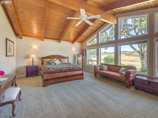 bedroom with ceiling fan, multiple windows, carpet floors, and beamed ceiling