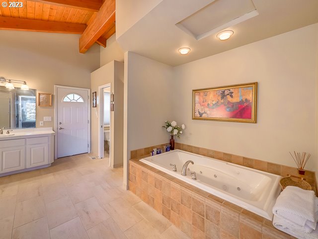 bathroom with wooden ceiling, vaulted ceiling with beams, toilet, tiled tub, and vanity