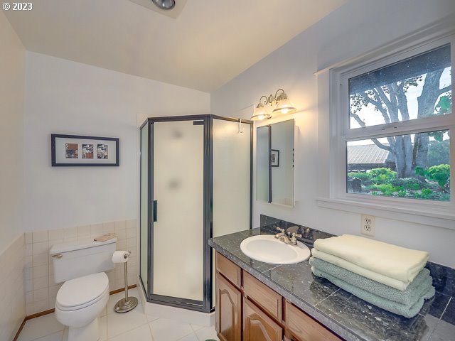 bathroom with toilet, tile patterned flooring, tile walls, a shower with shower door, and vanity