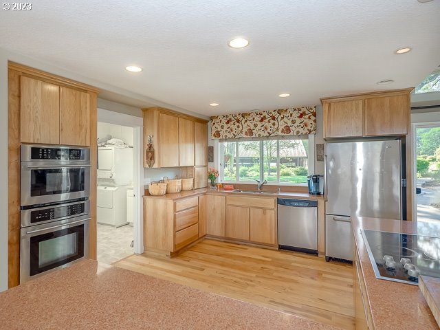 kitchen featuring a wealth of natural light, stacked washer and dryer, light brown cabinetry, light wood-type flooring, and appliances with stainless steel finishes