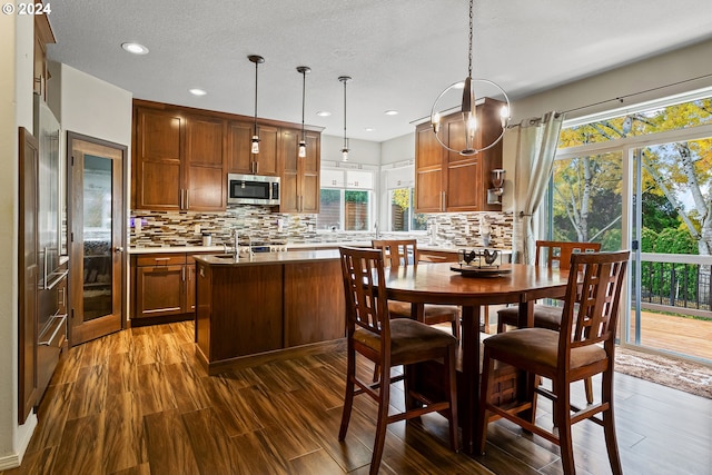 kitchen with decorative backsplash, decorative light fixtures, a kitchen island with sink, and dark wood-type flooring