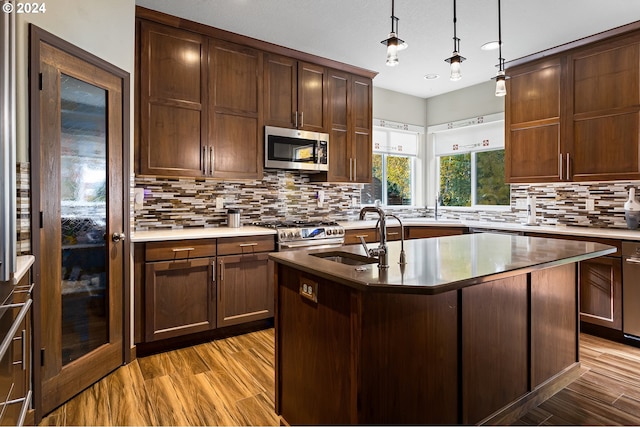 kitchen with backsplash, a kitchen island with sink, sink, light wood-type flooring, and stainless steel appliances