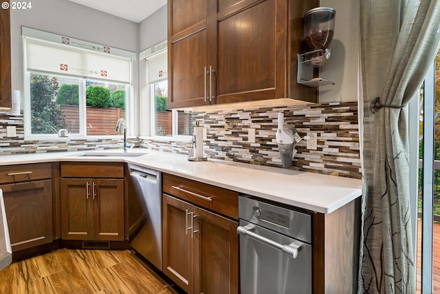 kitchen with tasteful backsplash, sink, dishwasher, and light hardwood / wood-style flooring