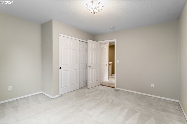 unfurnished bedroom featuring a textured ceiling, light colored carpet, and a closet