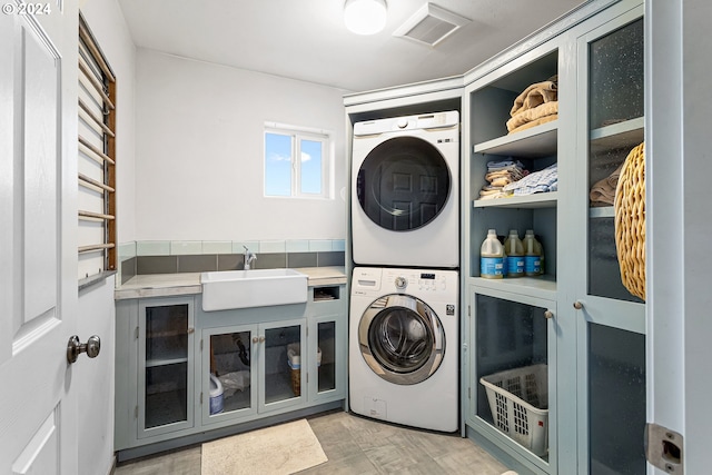 laundry room with stacked washer / dryer, sink, and cabinets