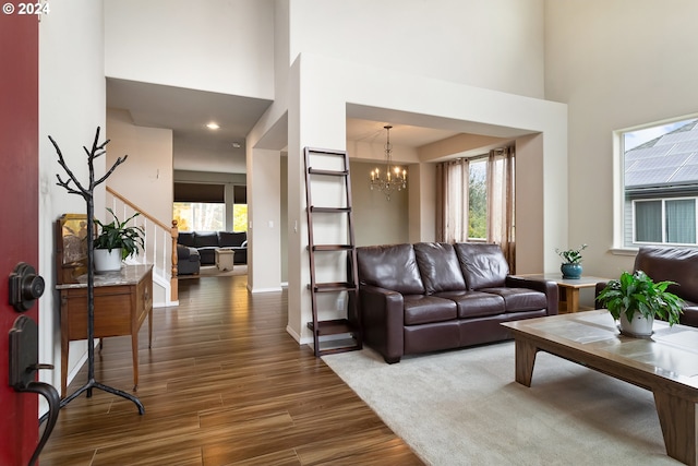 living room featuring plenty of natural light, a towering ceiling, dark hardwood / wood-style floors, and an inviting chandelier