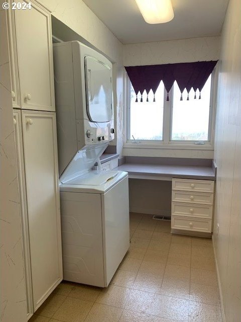 washroom with stacked washer and clothes dryer and cabinets