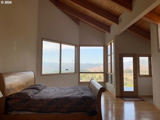 bedroom featuring light wood-type flooring, a mountain view, wooden ceiling, beam ceiling, and access to outside