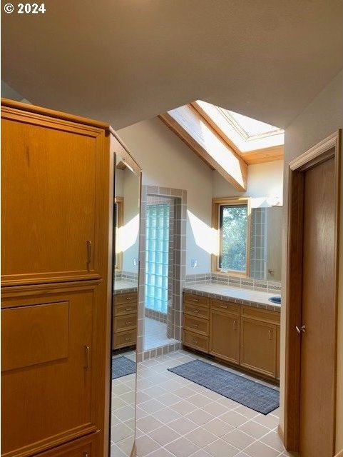 bathroom with lofted ceiling with skylight, tile patterned flooring, and vanity