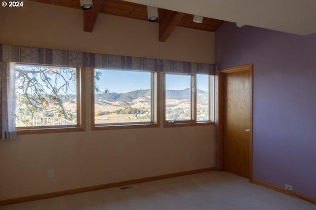 empty room featuring beamed ceiling, a mountain view, and a healthy amount of sunlight